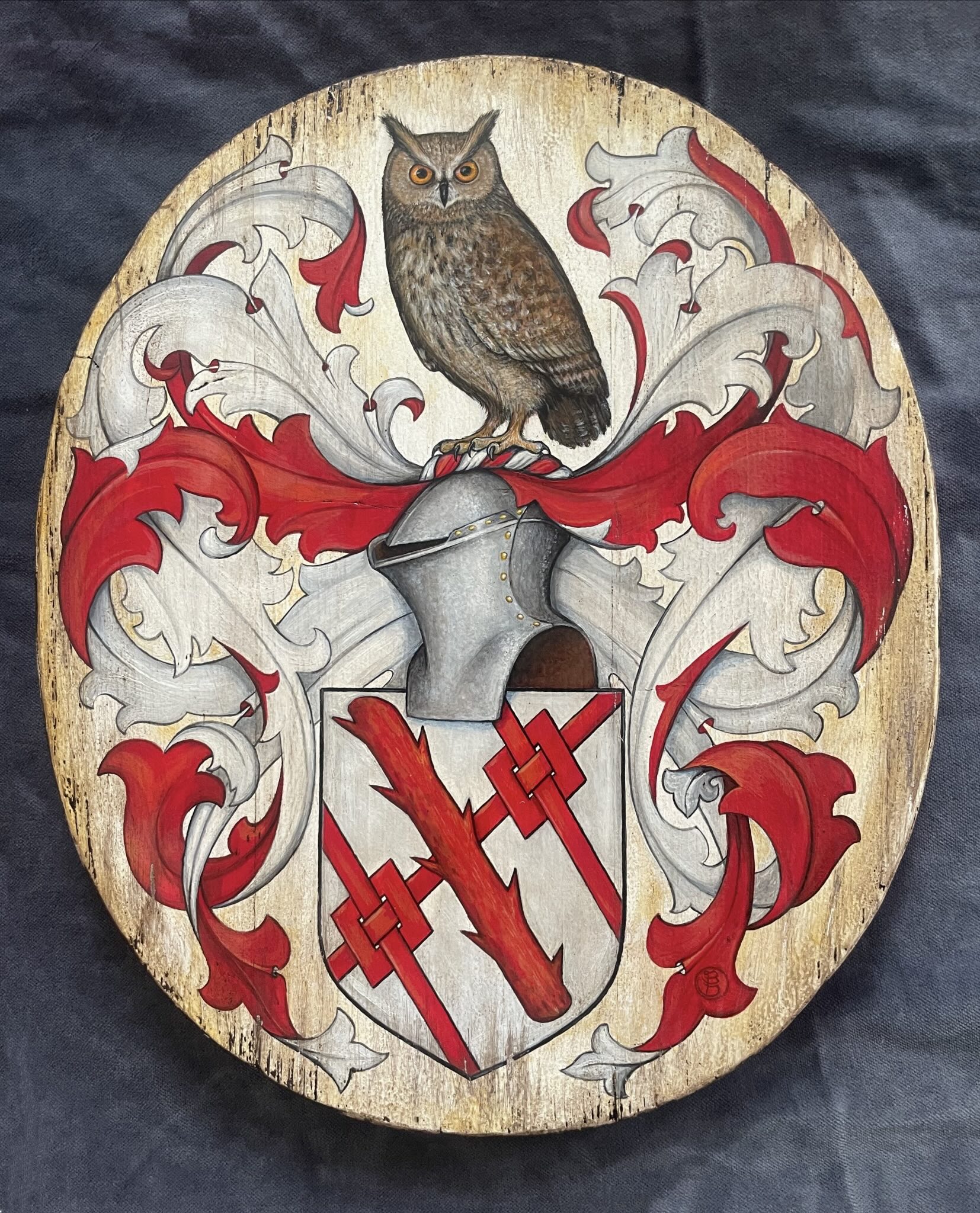 Hand-painted wooden coat of arms shield with an owl crest atop a knight's helm, red and silver mantling, and a shield bearing an interlaced cross design